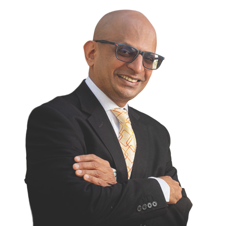 A smiling man with glasses stands confidently with arms crossed. He wears a black suit and patterned yellow tie, set against a plain white background.