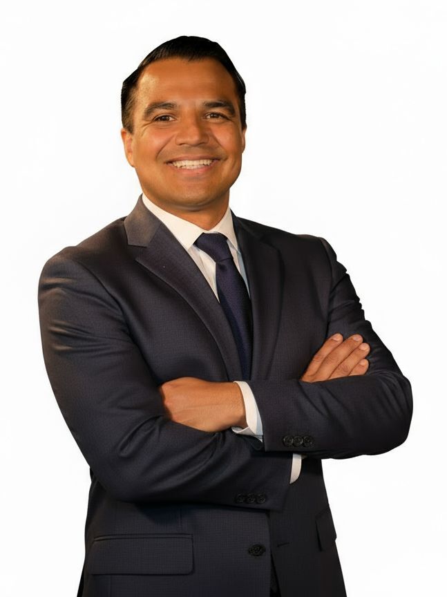 Smiling man in a dark suit with crossed arms, against a black background, conveying confidence and professionalism.