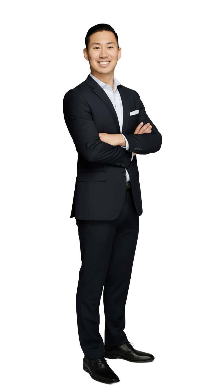 A man in a dark suit stands confidently with arms crossed against a black background. He smiles warmly, conveying a professional and approachable demeanor.