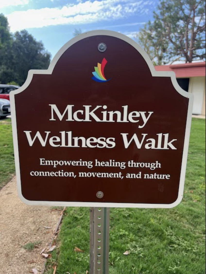 Sign for "McKinley Wellness Walk" in a grassy area. Text reads: "Empowering healing through connection, movement, and nature." Calm and inviting tone.