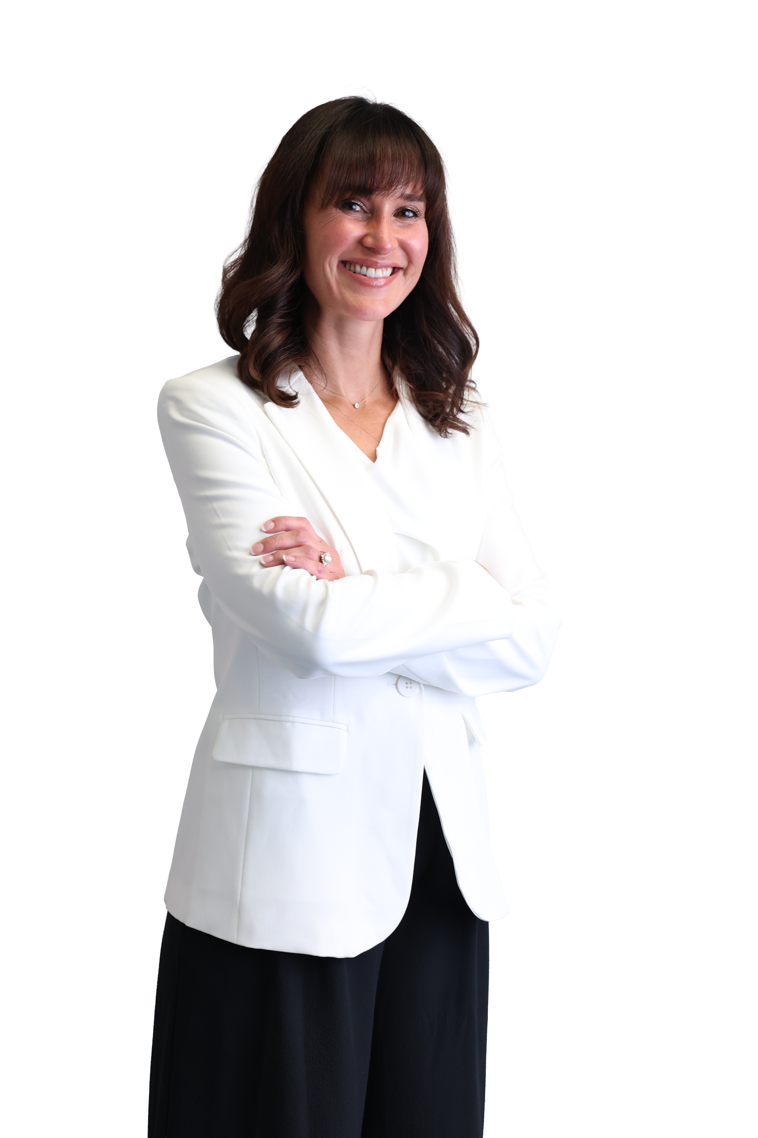 Smiling woman with brown hair, wearing a white blazer and black pants, stands confidently with arms crossed against a plain black background.